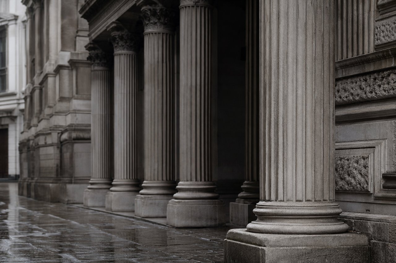 Stone facade detail of a Victorian London exchange building, fluted columns and deep shadow under the portico in overcast light