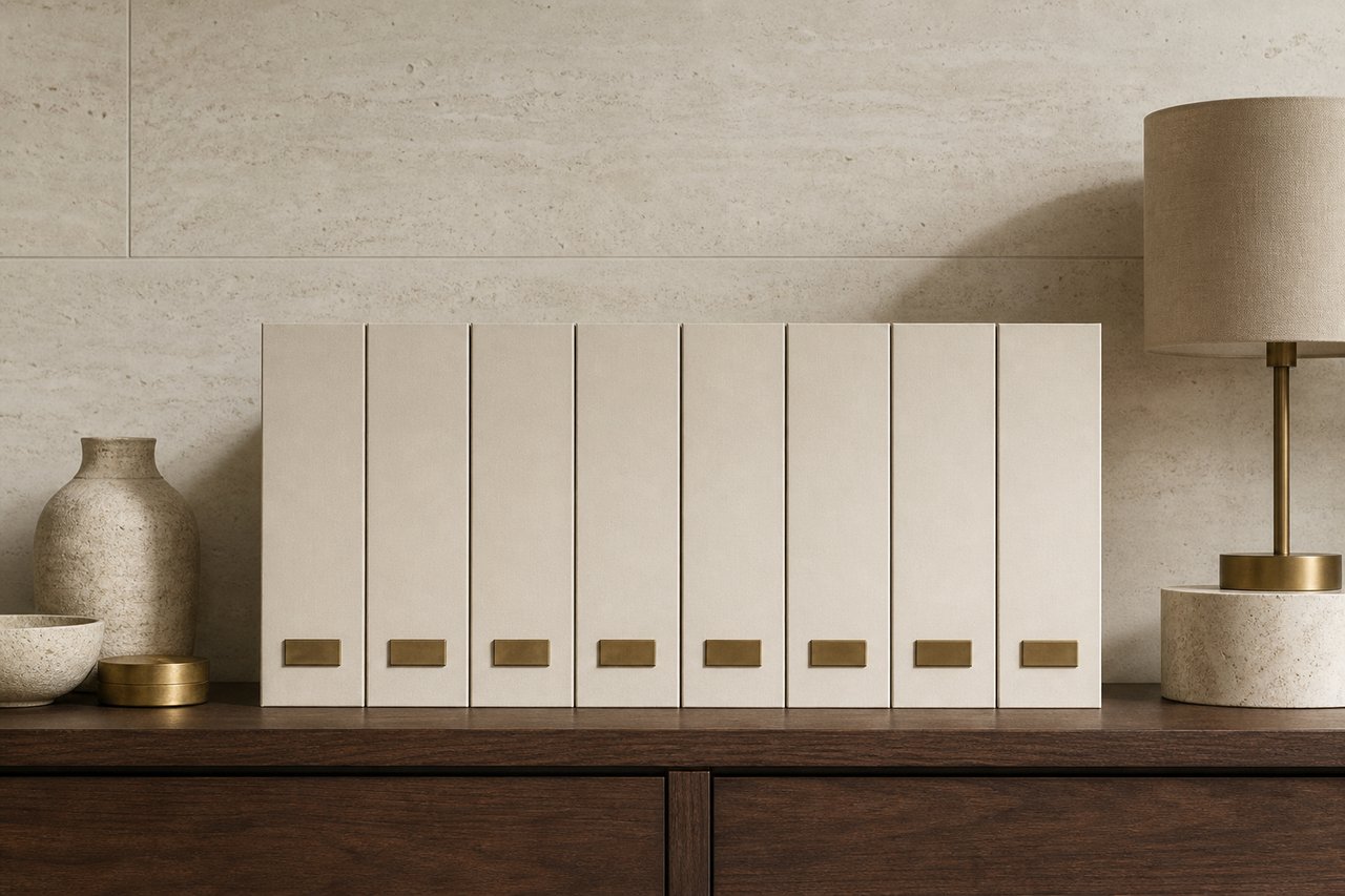 A row of eight identical unlabelled cream archive box files standing shoulder to shoulder on a dark walnut sideboard